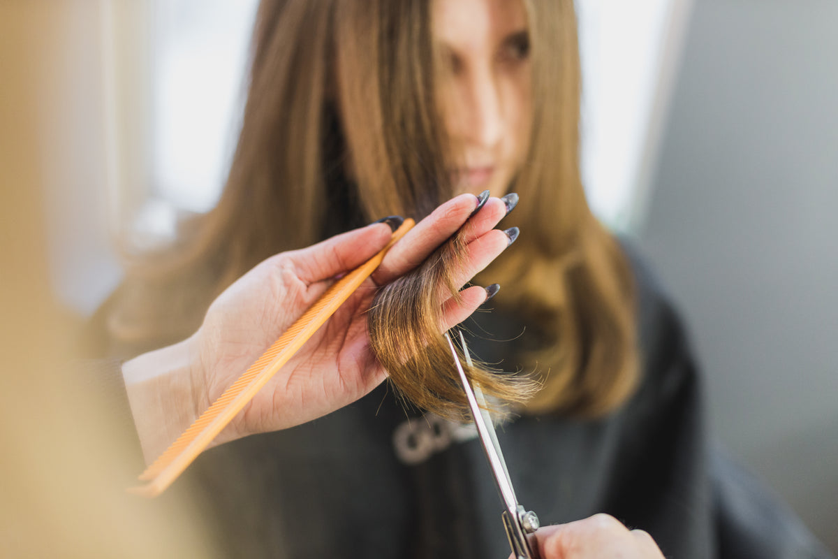 Stylist trimming the ends of a client’s long brown hair with scissors and a comb